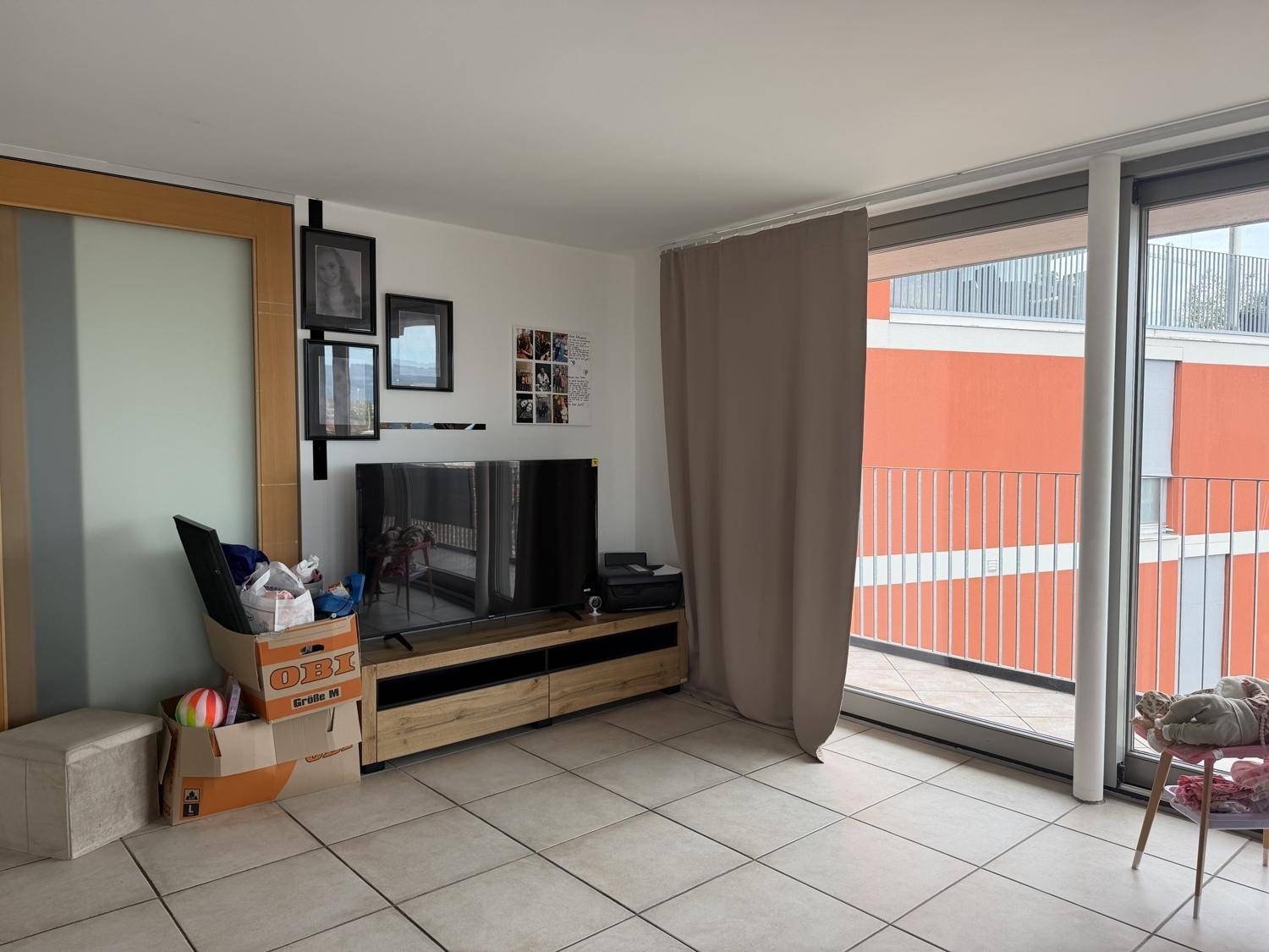 Gemütlicher Wohnbereich mit Fernseher und großen Schiebetüren, die zum Balkon führen.