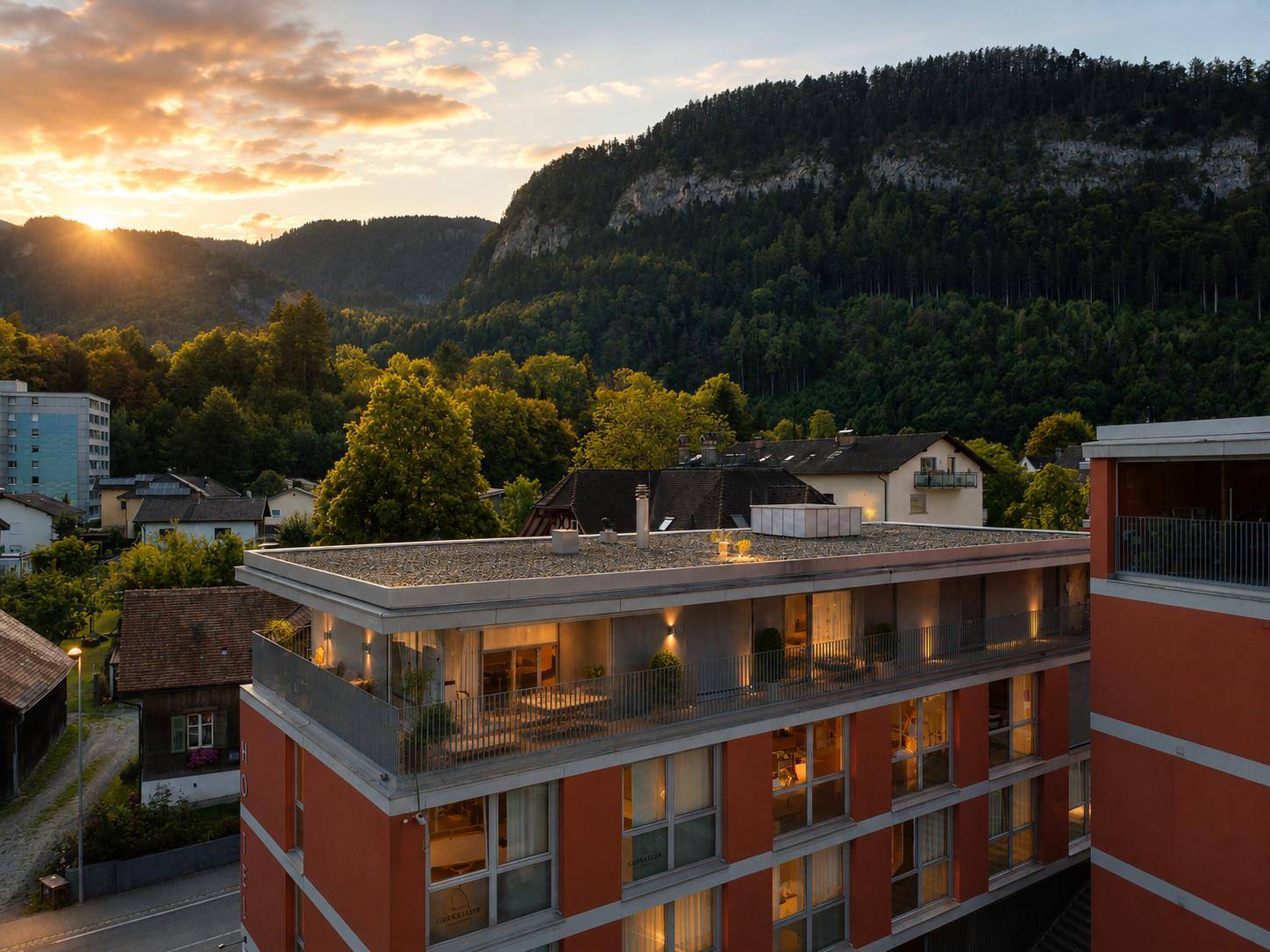 Moderne Wohnanlage mit Flachdach und Balkonen vor einer malerischen Bergkulisse bei Sonnenuntergang.