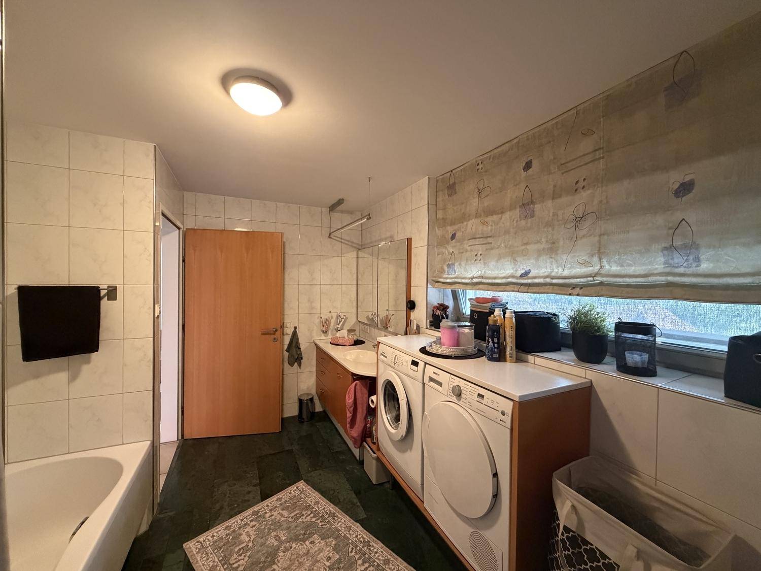 Helles Badezimmer mit Badewanne, Waschmaschine und Trockner, sowie einem Fenster für Tageslicht.