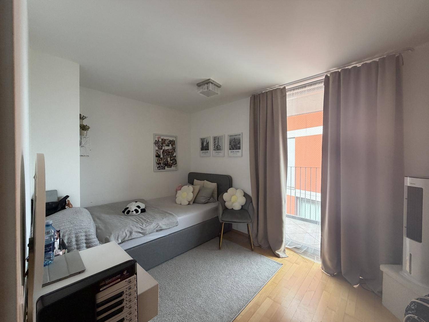 Helles Schlafzimmer mit Einzelbett, Holzboden und großem Fenster mit Zugang zum Balkon.