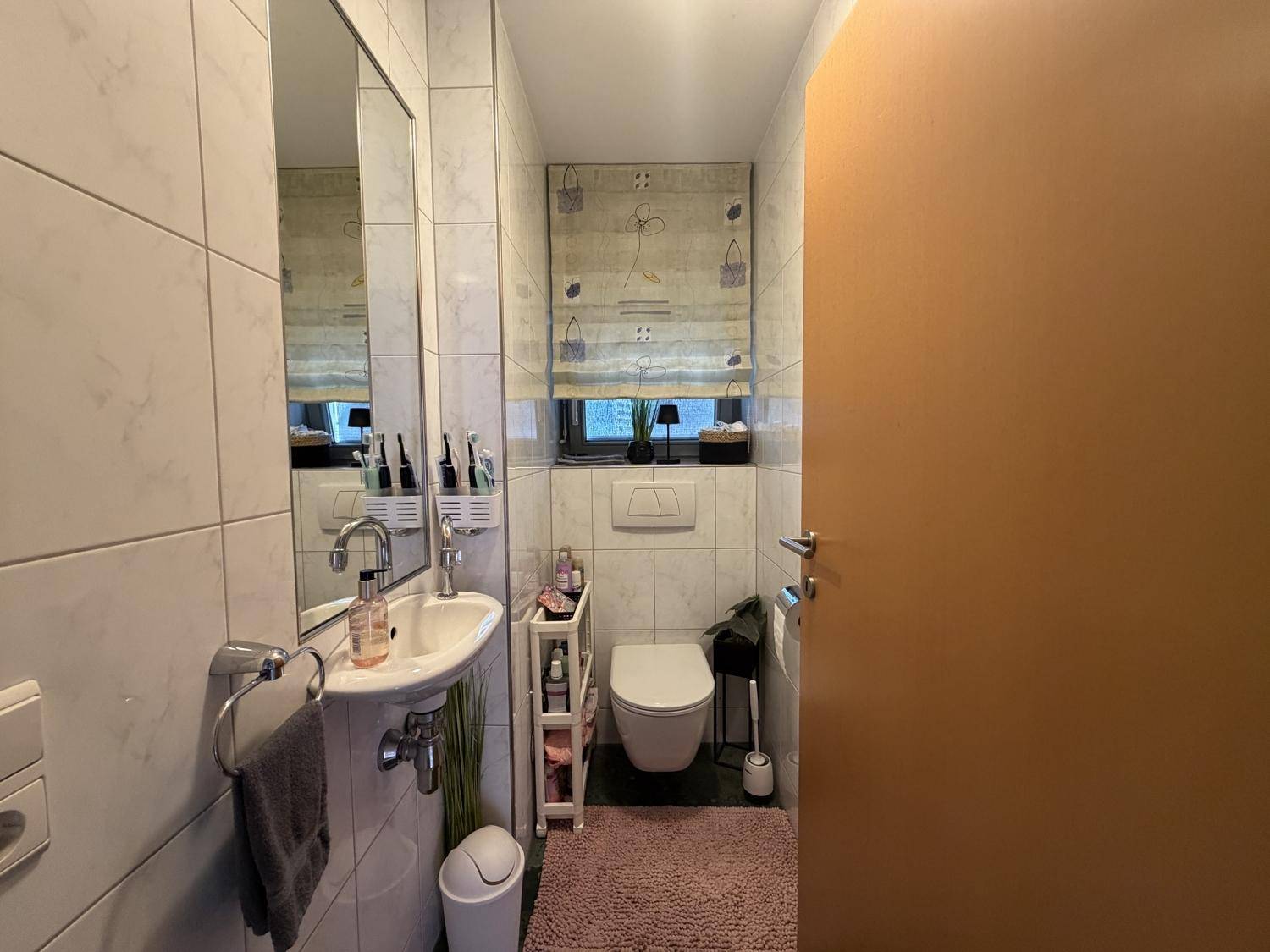 Kleines Gäste-WC mit weißen Fliesen, wandhängendem WC und kleinem Waschbecken.