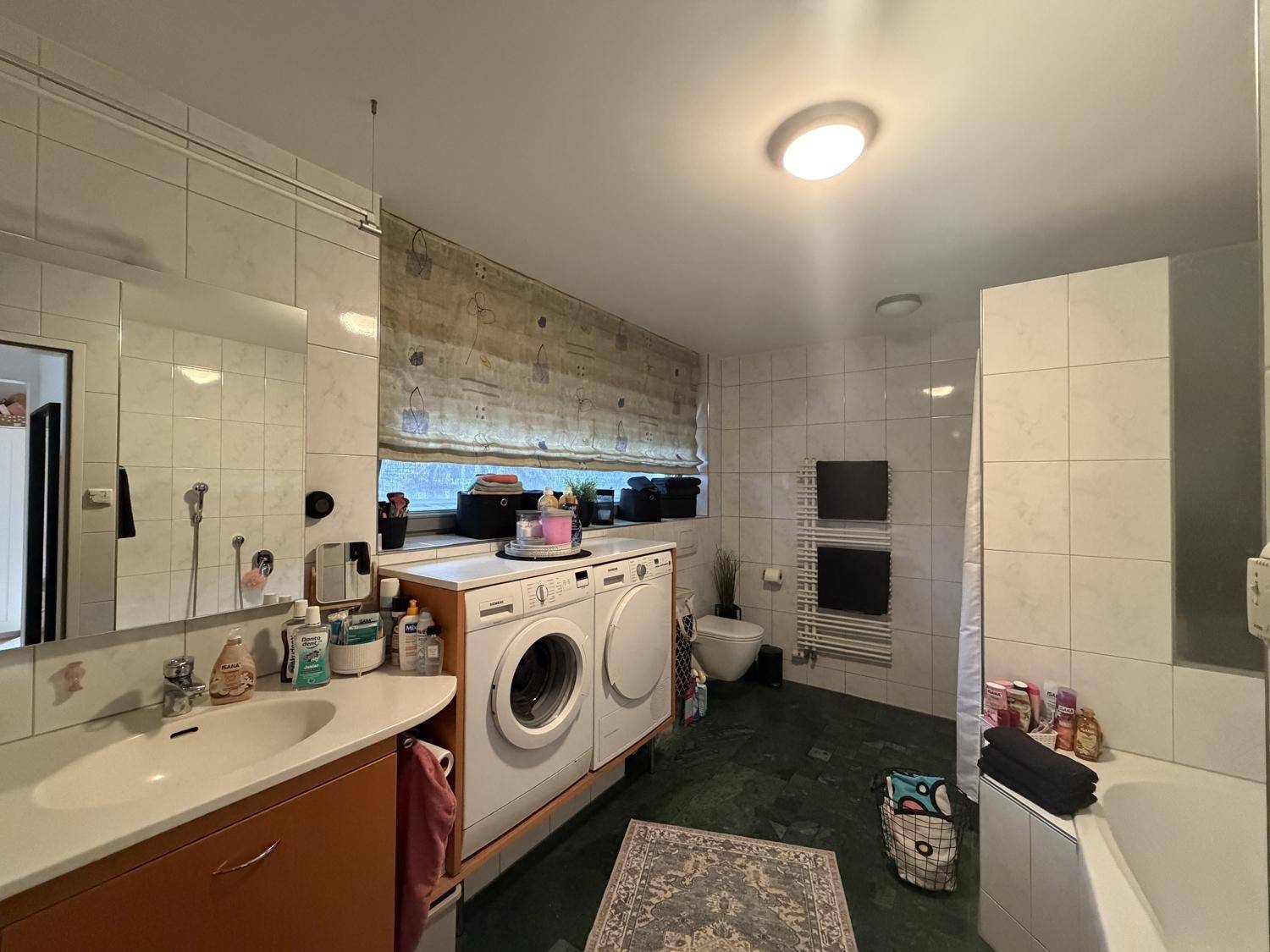 Geräumiges Badezimmer mit Badewanne, Waschmaschine, Trockner und beheiztem Handtuchhalter.