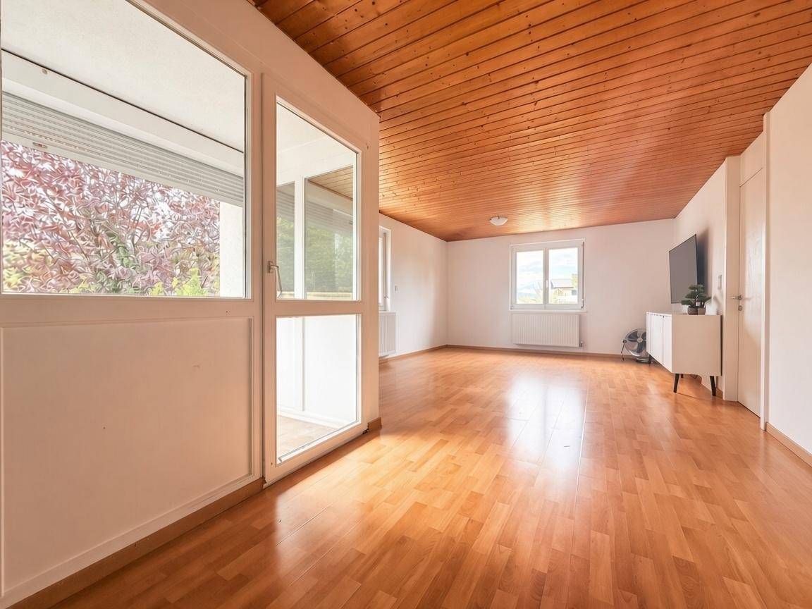 Geräumiges Wohnzimmer mit hellem Parkettboden, Holzdecke und großen Fenstern für viel Tageslicht.