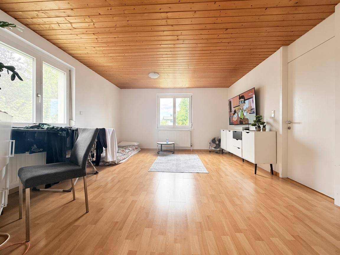 Heller Wohnbereich mit Holzdecke und Parkettboden, ausgestattet mit einem Fernseher und einem kleinen Teppich.