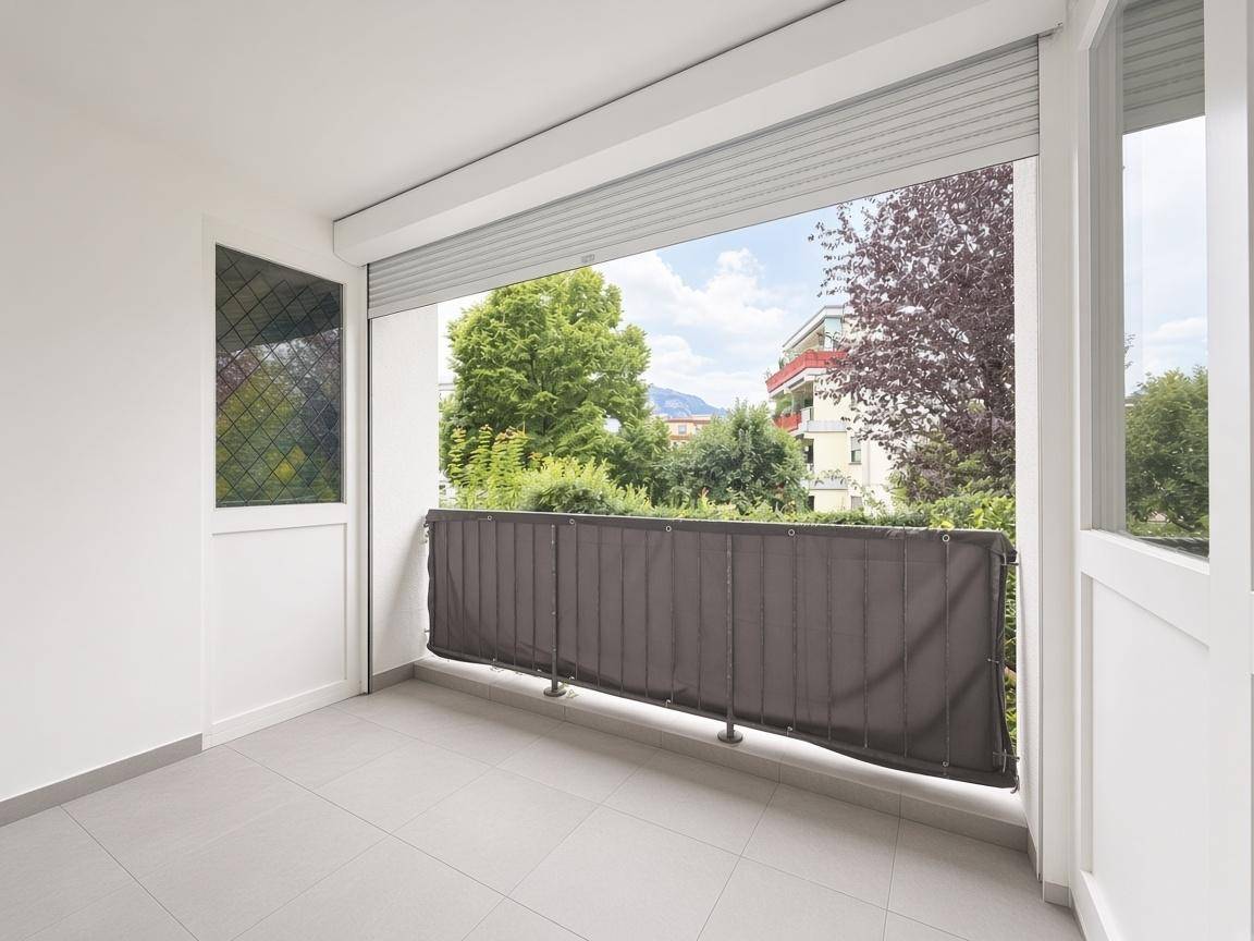 Überdachter Balkon mit Fliesenboden, Sichtschutz und Blick auf die Umgebung.