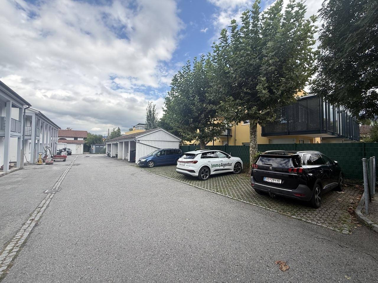 Außenbereich mit Parkplätzen, Garagen und Bäumen unter bewölktem Himmel.