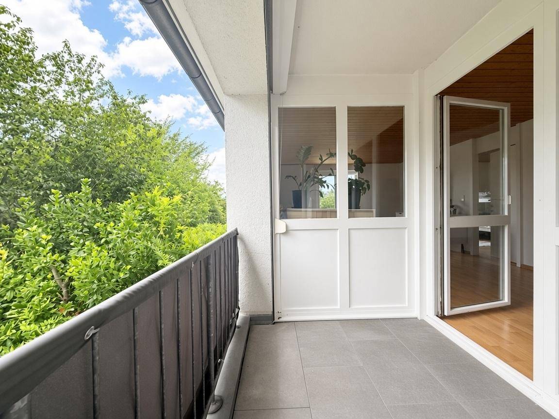 Heller Balkon mit Fliesenboden und Blick ins Grüne, zugänglich vom Innenbereich.