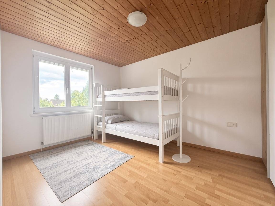 Kinderzimmer mit Etagenbett, hellem Parkettboden und einem Fenster, das viel Tageslicht hereinlässt.