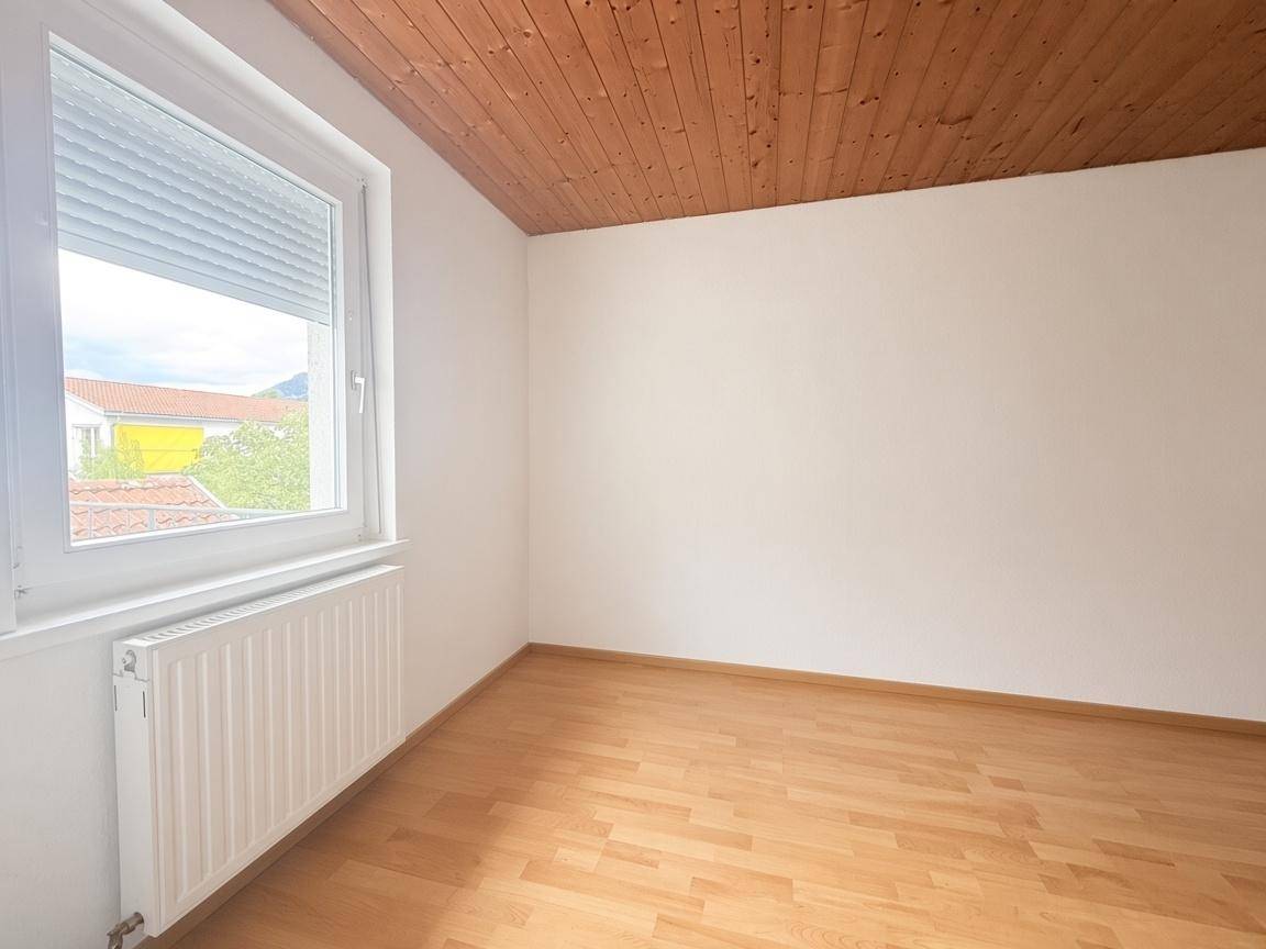 Helles Schlafzimmer mit Parkettboden, Holzdecke und einem Fenster mit Rollladen.