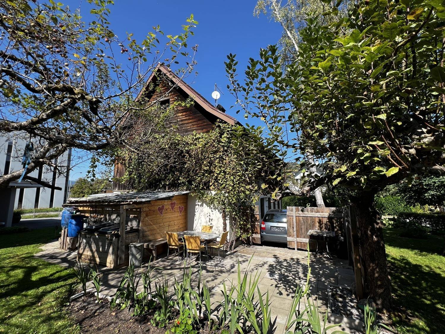 Gartenbereich mit gepflastertem Sitzplatz, Grillmöglichkeit und üppiger Vegetation am Haus.