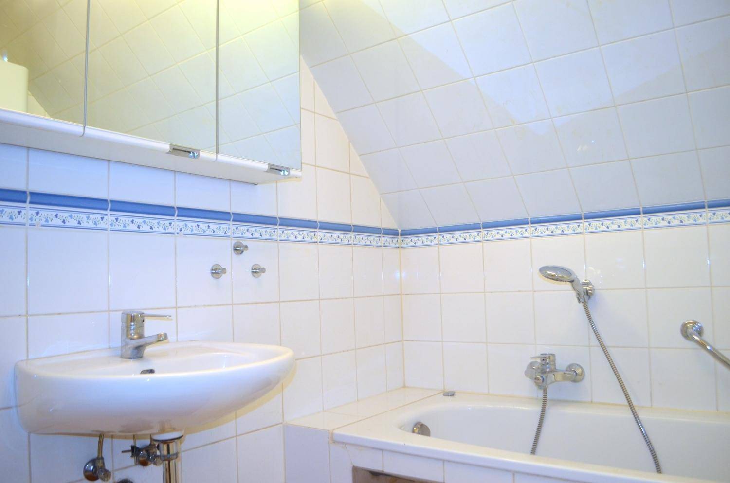Badezimmer mit Badewanne, Waschbecken, Dachschräge und weißen Fliesen mit blauer Bordüre.