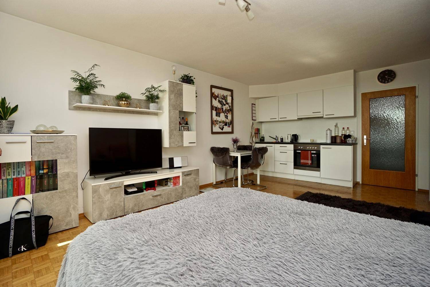 Studio-Apartment mit Schlafbereich, TV-Ecke und integrierter Küchenzeile im Hintergrund.