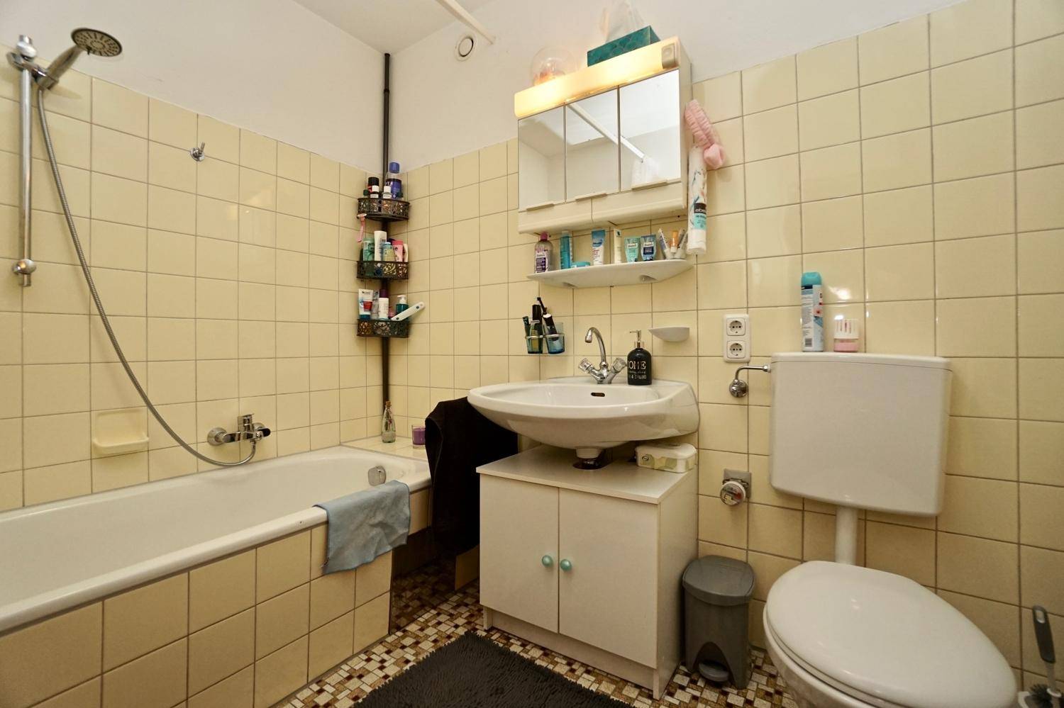 Badezimmer mit gelben Fliesen, Badewanne mit Duschfunktion, Waschbecken und Toilette.