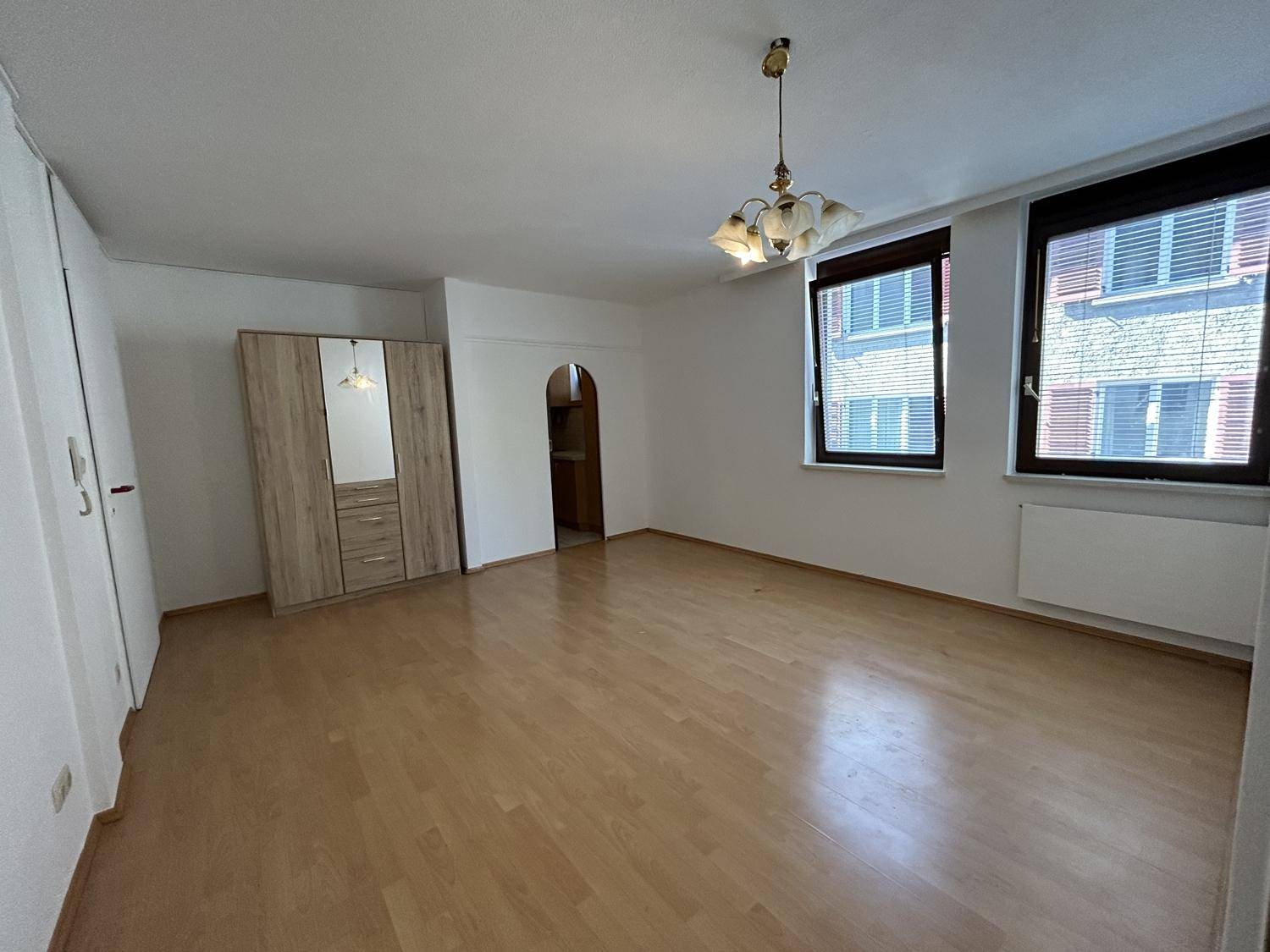 Geräumiger Wohnbereich mit hellem Laminatboden und zwei Fenstern, gut beleuchtet.