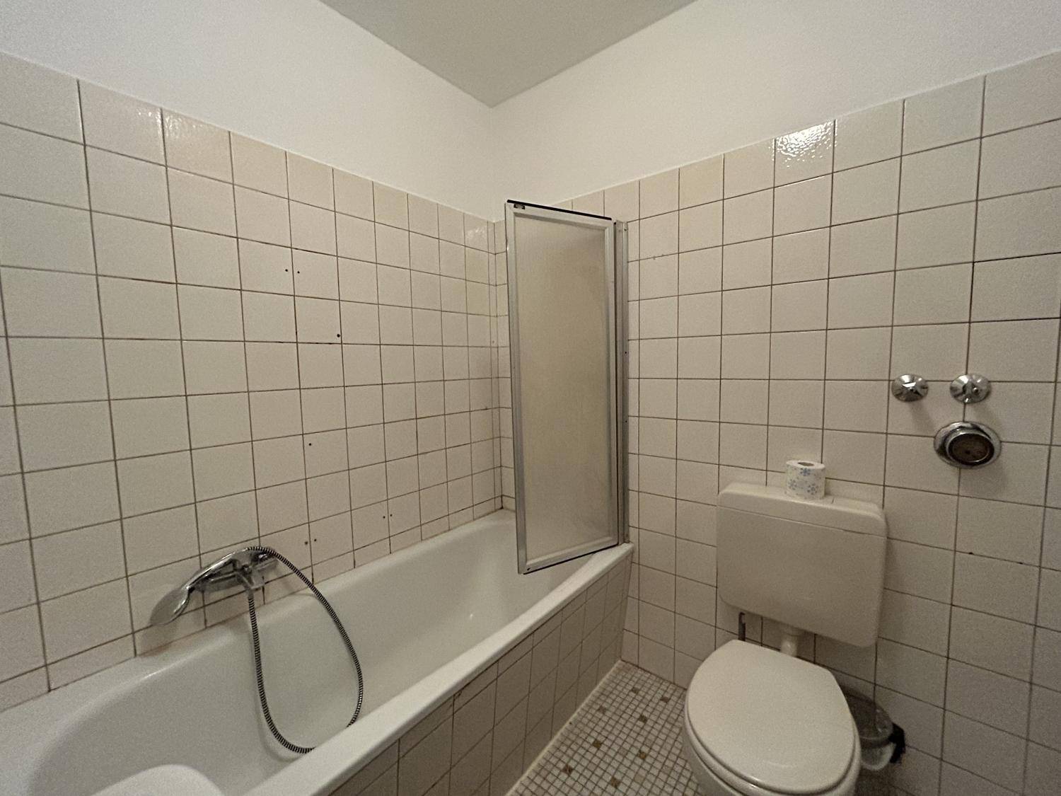 Badezimmer im 80er-Jahre-Stil mit Badewanne, Duschabtrennung und WC, gefliest.