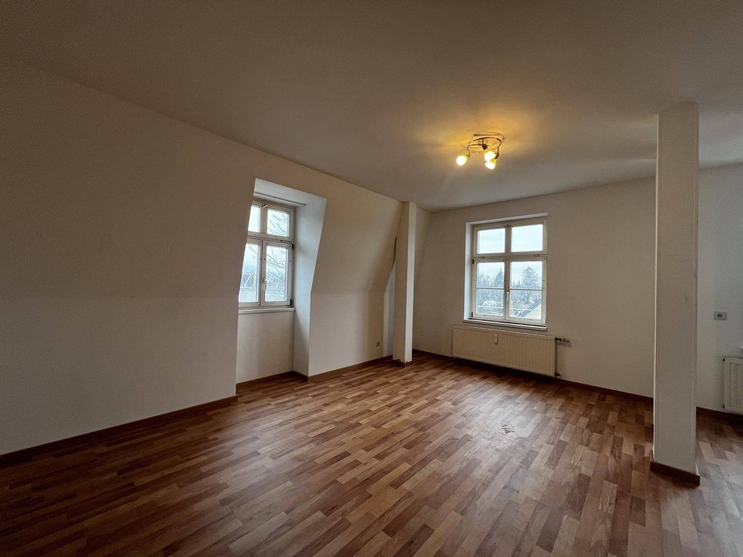 Heller Raum mit Holzboden, einem Fenster und charakteristischer Dachschräge, ideal für individuelle Gestaltung.