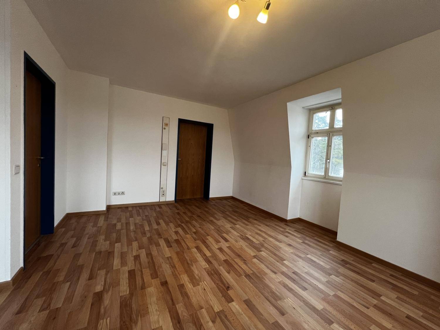 Leerer Raum mit Holzboden, zwei Türen und einem Fenster, bereit zur individuellen Gestaltung im Dachgeschoss.