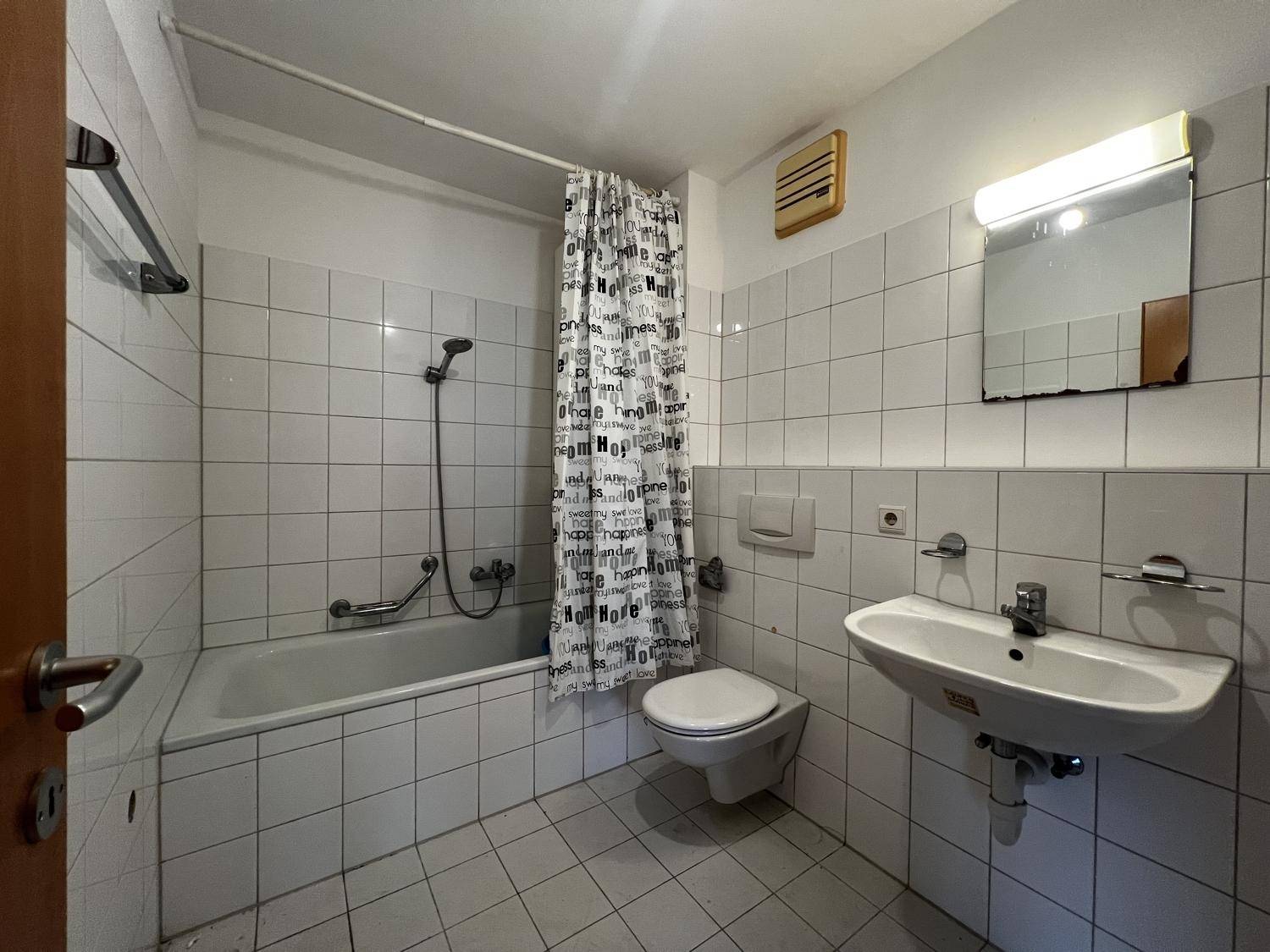 Funktionales Badezimmer mit weißen Fliesen, Badewanne mit Duschvorhang und Waschbecken.