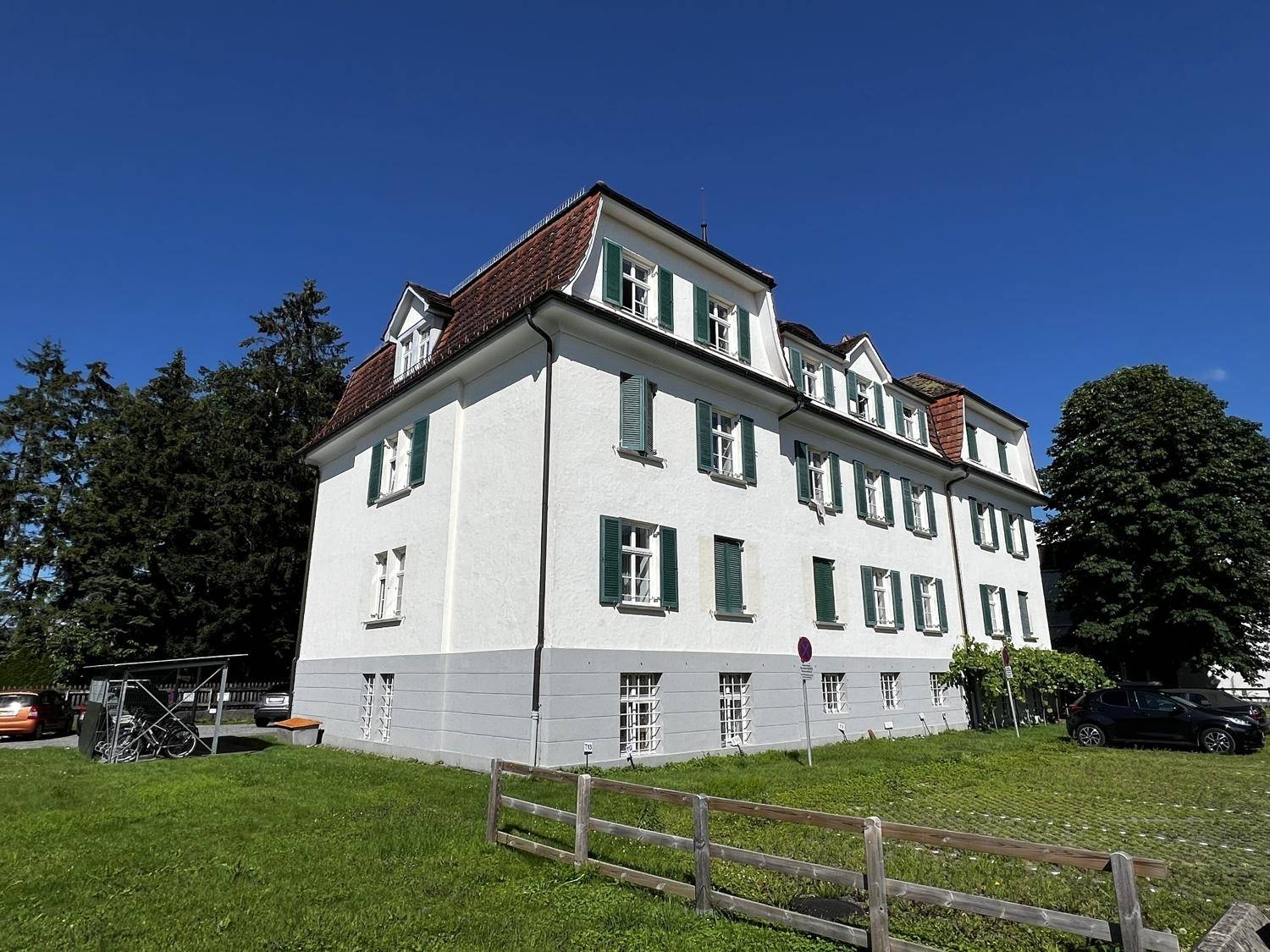 Historisches Gebäude mit weißer Fassade, grünen Fensterläden und Mansarddach unter blauem Himmel.