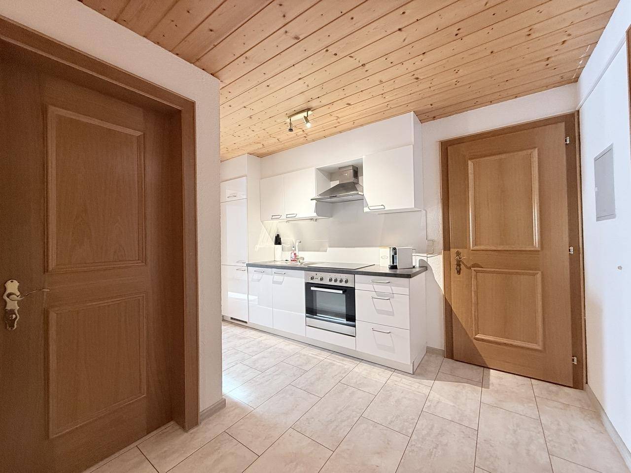 Heller Flur mit Holztüren und Fliesenboden, der zu einer modernen weißen Küche führt.