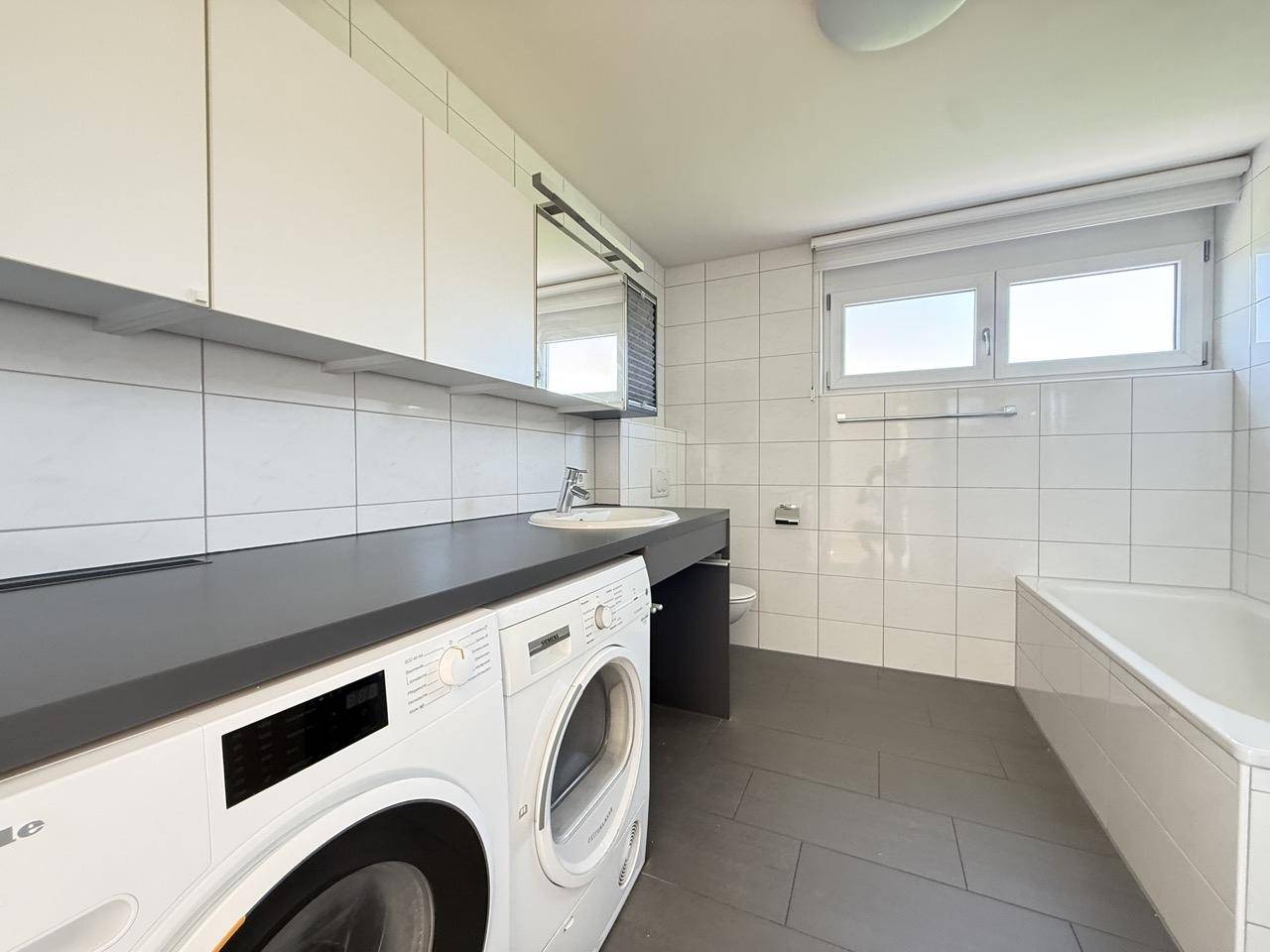 Funktionales Badezimmer mit Fenster, Waschbecken, Toilette und integrierten Schränken.