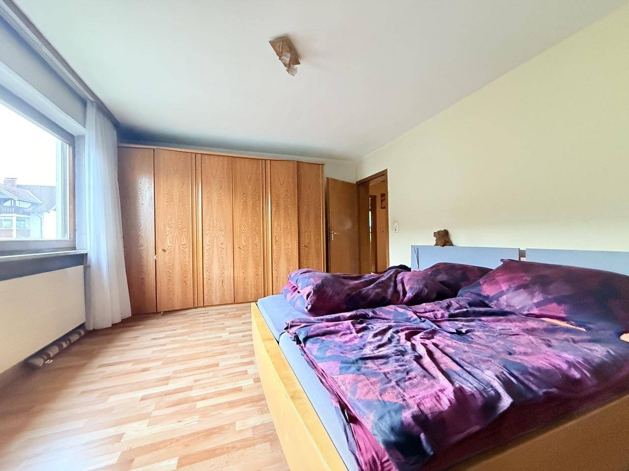 Schlafzimmer mit Laminatboden, großem Holzschrank und Fenster, das viel Licht hereinlässt.