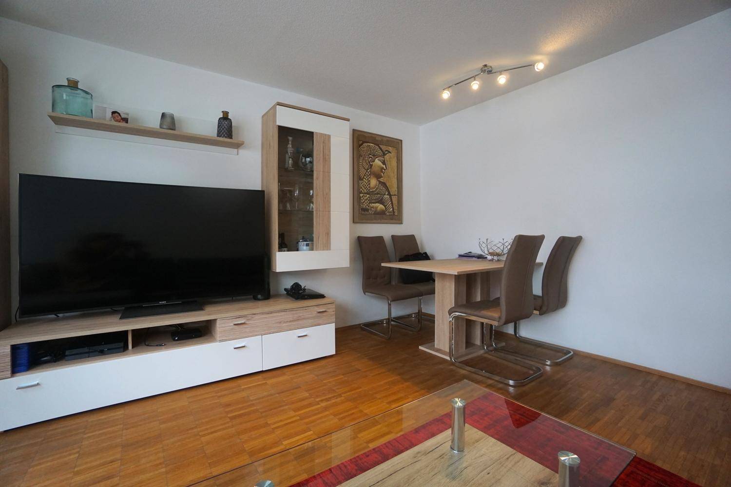 Essbereich mit Holztisch und passenden Stühlen, angrenzend an den Wohnbereich mit TV-Möbel.