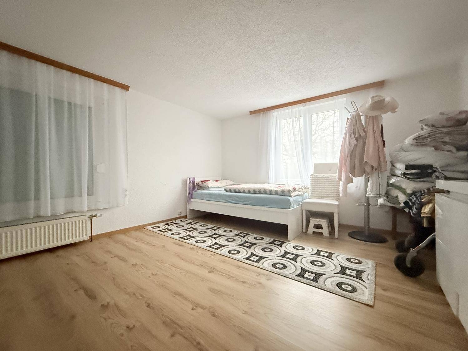Helles Schlafzimmer mit Holzboden, einem Bett und großem Fenster.