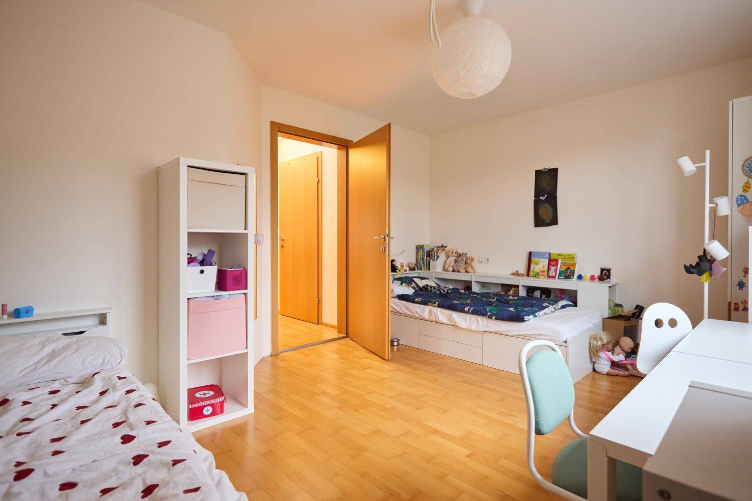 Helles Kinderzimmer mit zwei Betten, Stauraum und Holzboden.
