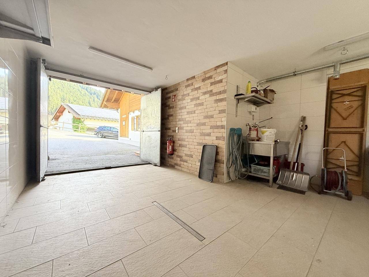 Helle Garage mit offenem Tor, Fliesenboden und Blick nach draußen.