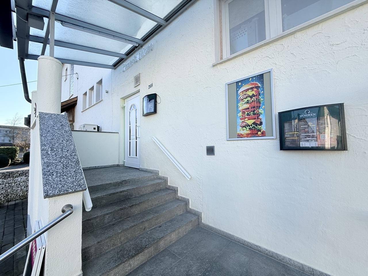 Eingangsbereich des Gebäudes mit Treppe, Überdachung und Werbeplakaten.