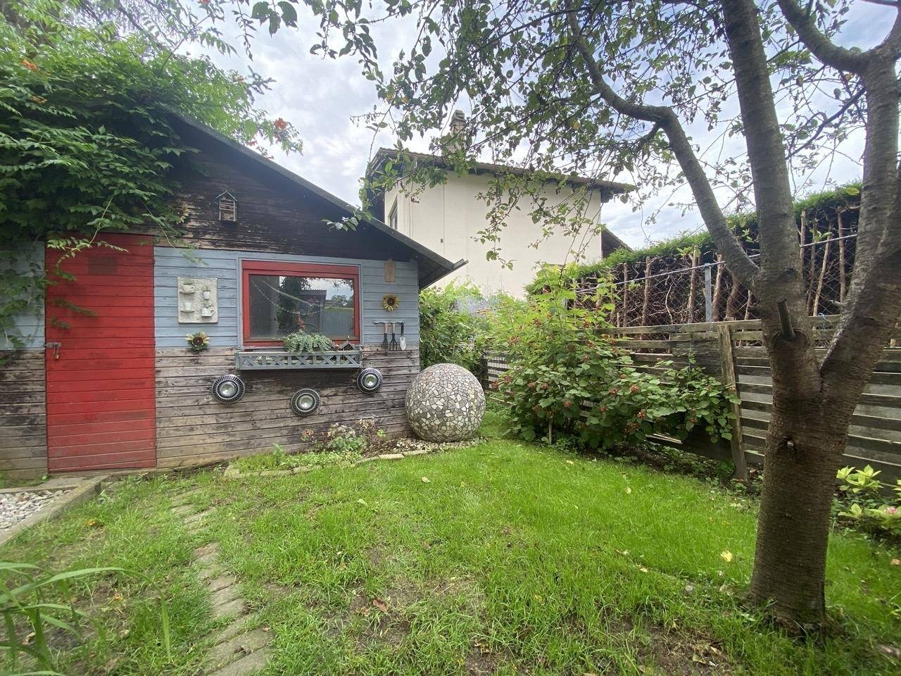 Gepflegter Gartenbereich mit Rasenfläche, Gartenhaus und Bäumen.