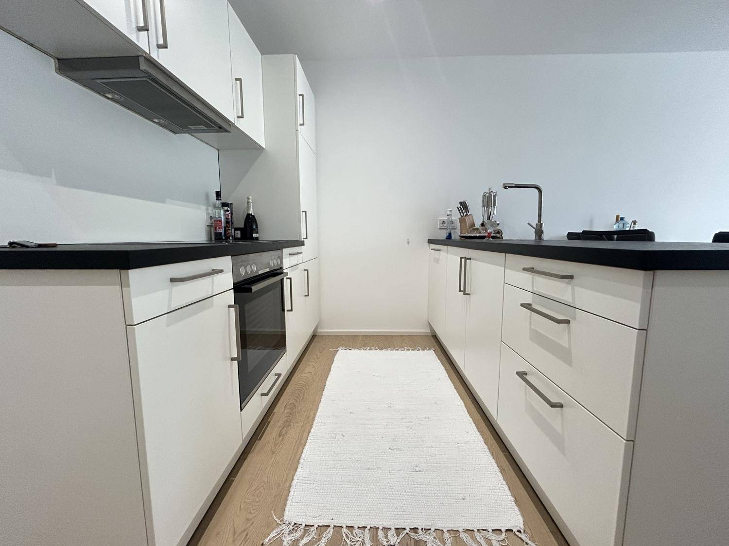 Moderne Einbauküche mit weißen Schränken, dunkler Arbeitsplatte und integriertem Backofen.