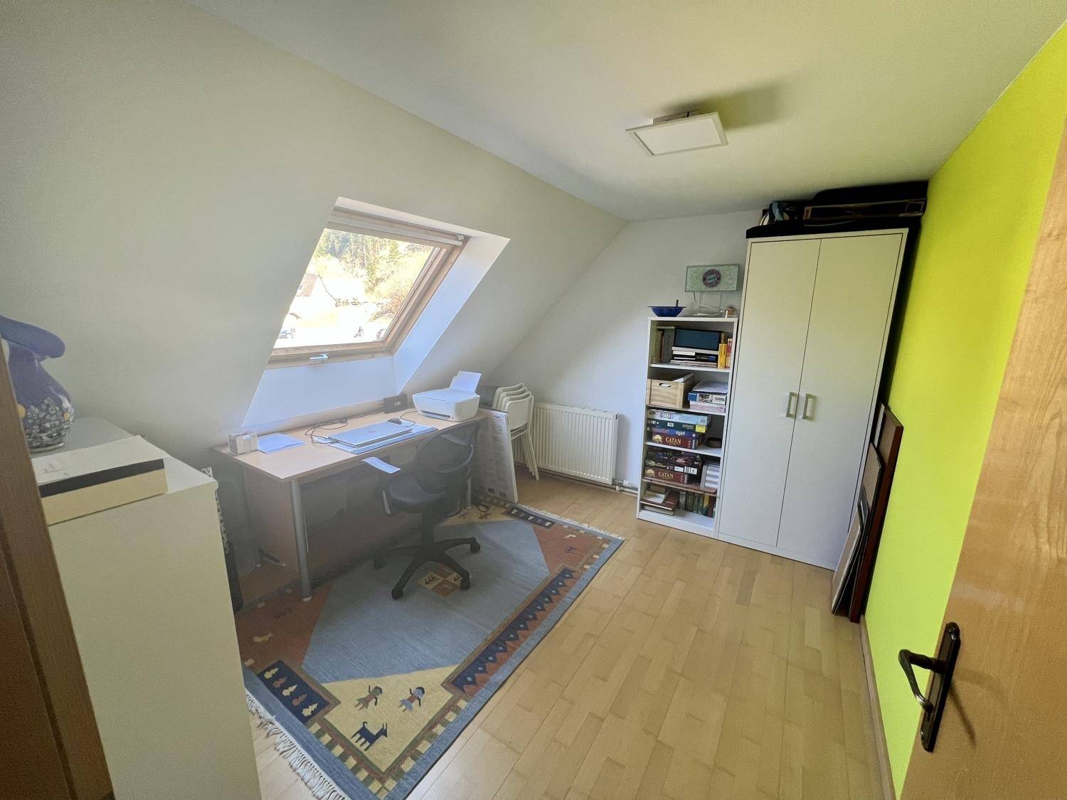 Helles Arbeitszimmer mit Dachschräge, Dachfenster, Schreibtisch und Teppichboden.