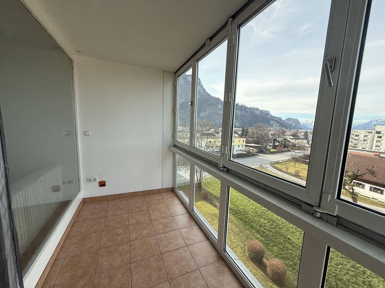 Verglaste Loggia mit Fliesenboden und beeindruckendem Blick auf die umliegende Berglandschaft und Stadt.