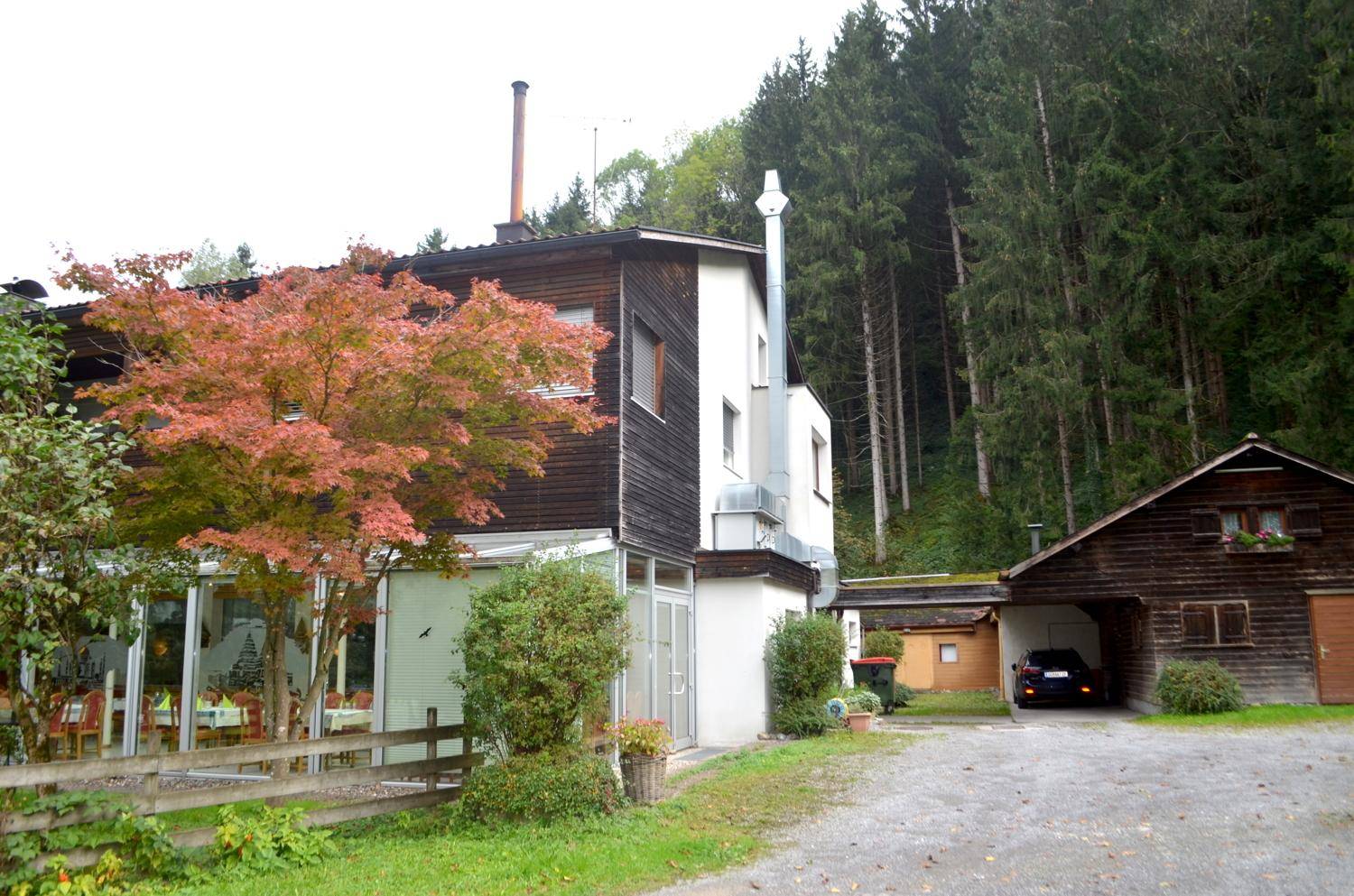 Rückansicht des Gebäudes mit Garage, umgeben von Bäumen und Natur.