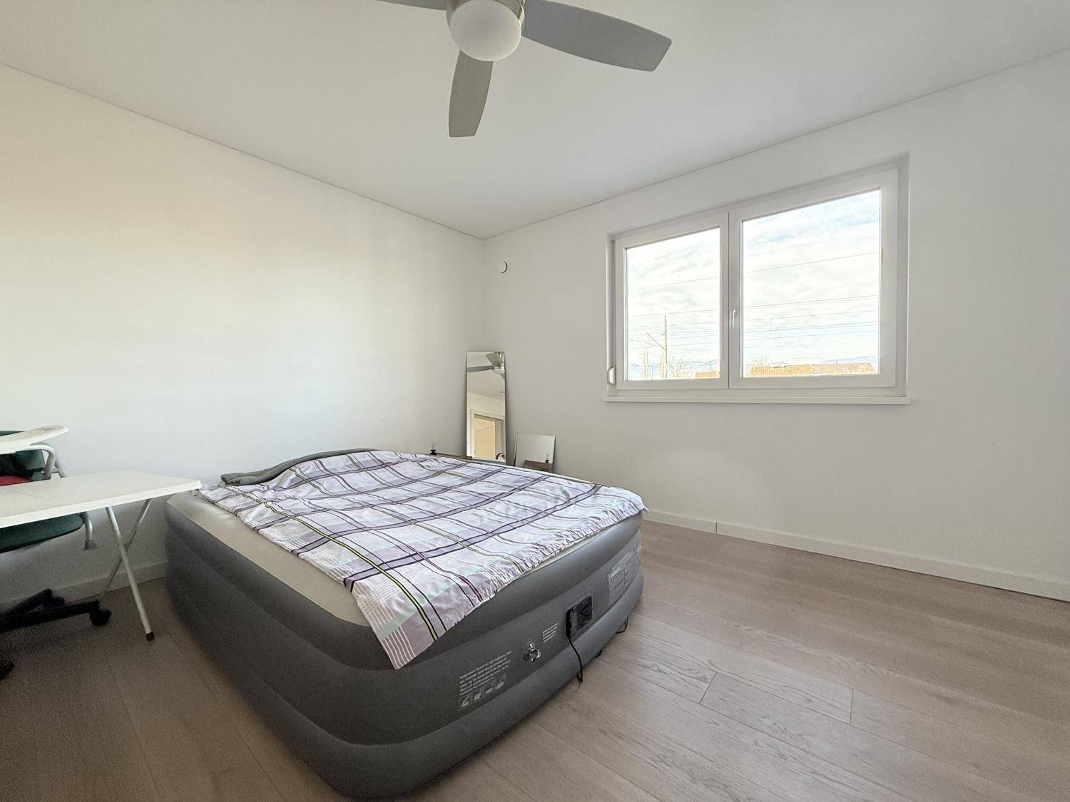 Helles Schlafzimmer mit großem Fenster und Holzboden.