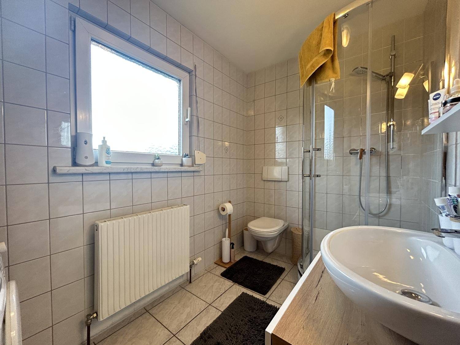 Gefliestes Badezimmer mit Duschkabine, WC, Waschbecken und Fenster für natürliche Belüftung.