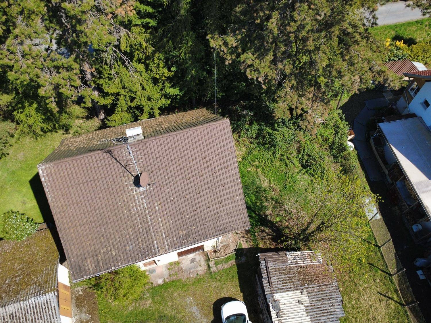 Blick von oben auf das Hausdach und die angrenzende bewaldete Umgebung.