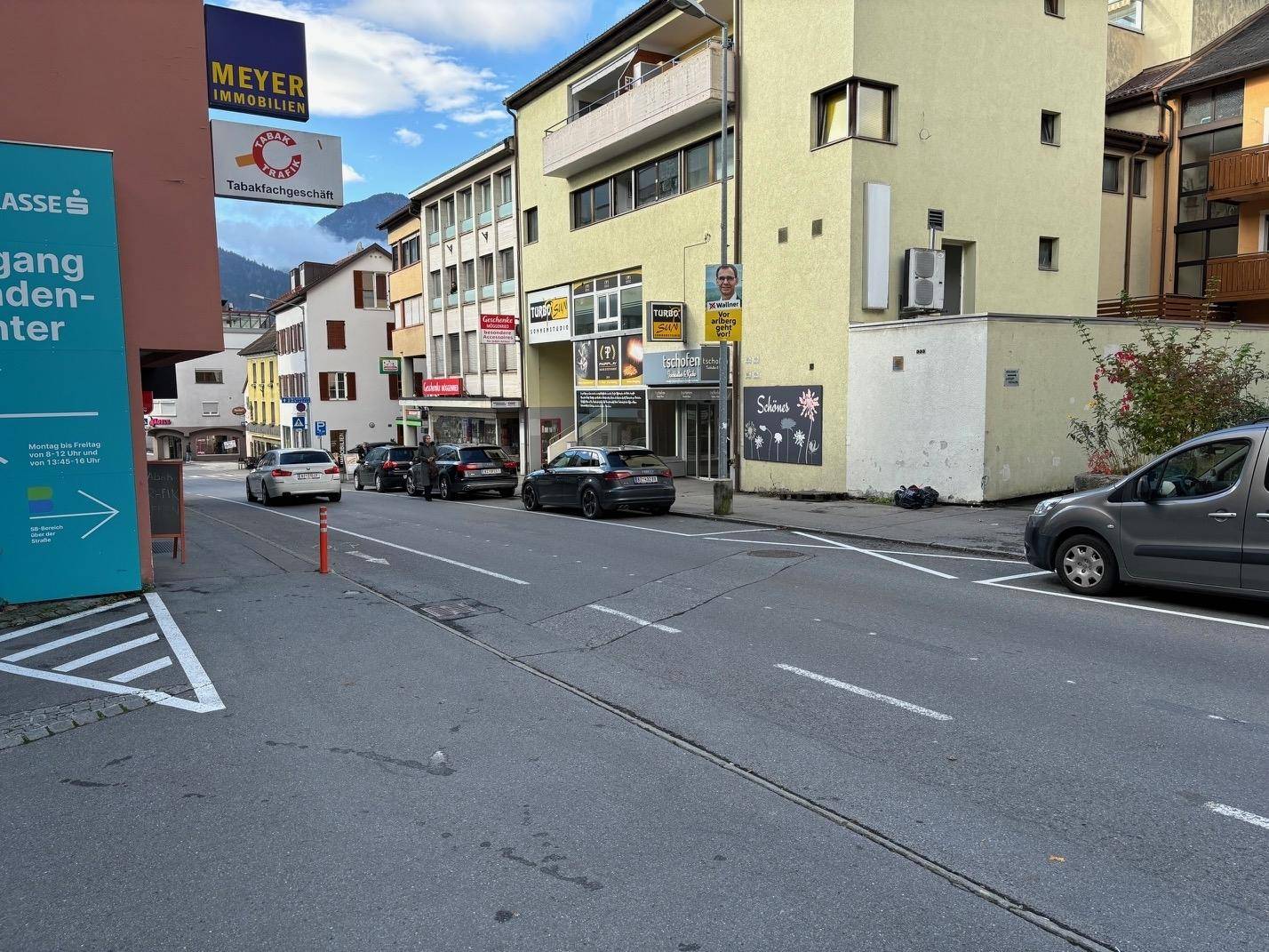 Straßenansicht mit parkenden Autos und dem Geschäftsgebäude im Hintergrund unter bewölktem Himmel.