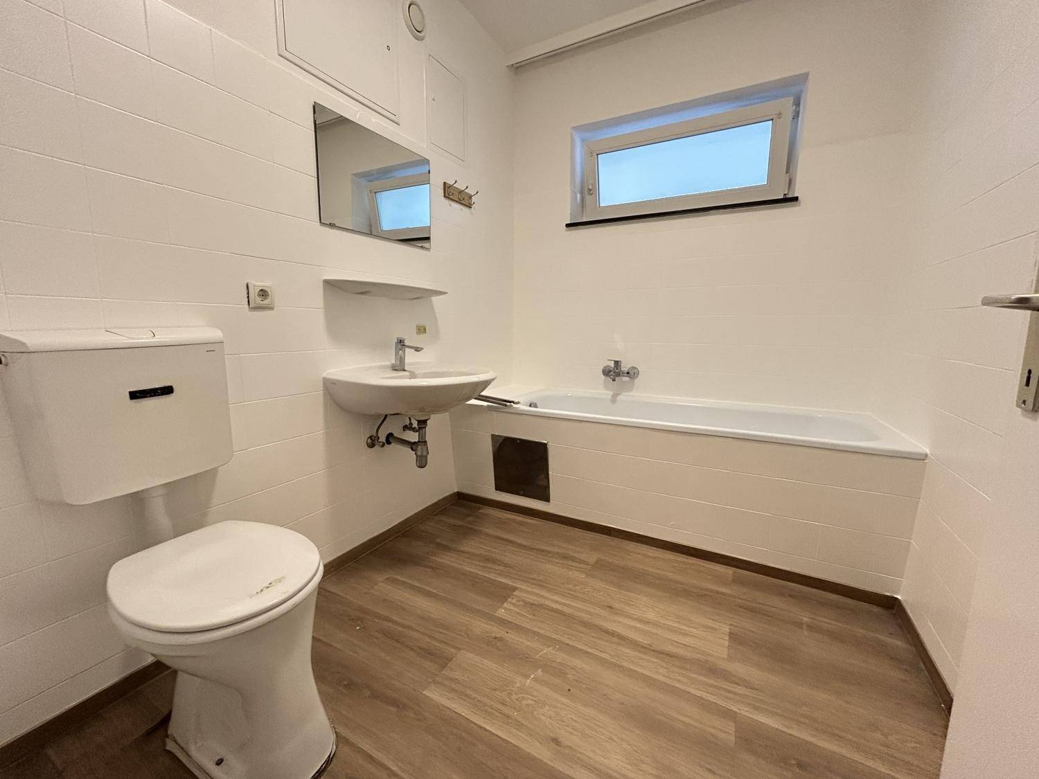 Helles Badezimmer mit Badewanne, WC, Waschbecken und Fenster für natürliche Belüftung.
