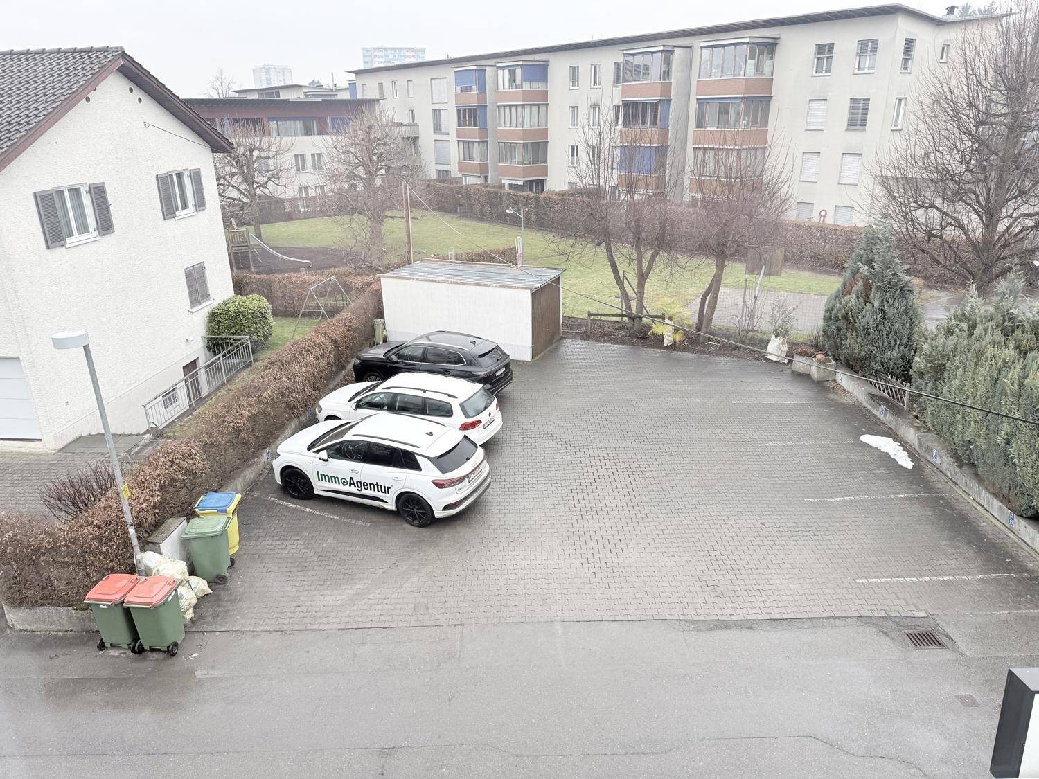 Großer gepflasterter Parkplatz mit mehreren Autos und angrenzenden Gebäuden.