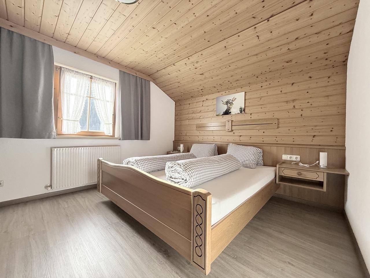 Gemütliches Schlafzimmer mit Holzverkleidung, Doppelbett und Fenster mit Blick nach draußen.