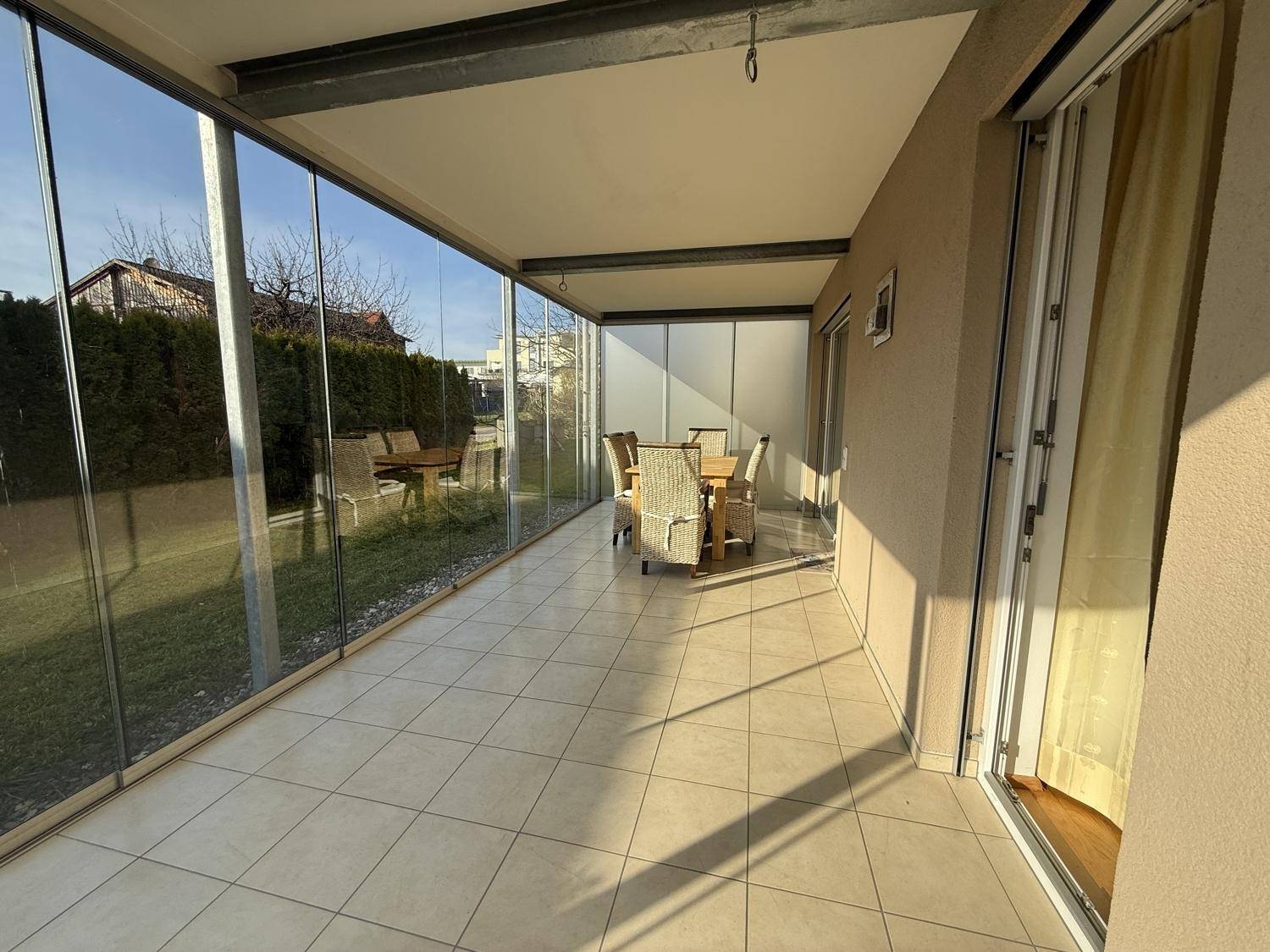 Geräumige, verglaste Terrasse mit Fliesenboden und Rattanmöbeln, ideal für Mahlzeiten im Freien.