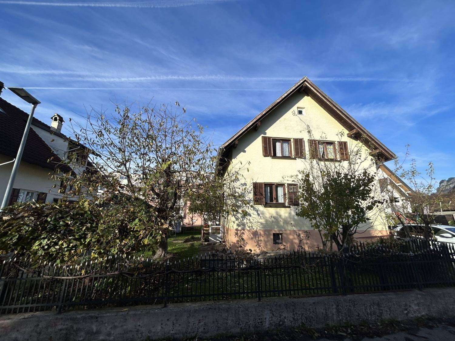 Seitenansicht des Hauses mit Zaun, Bäumen und Blick auf die umliegende Wohngegend.