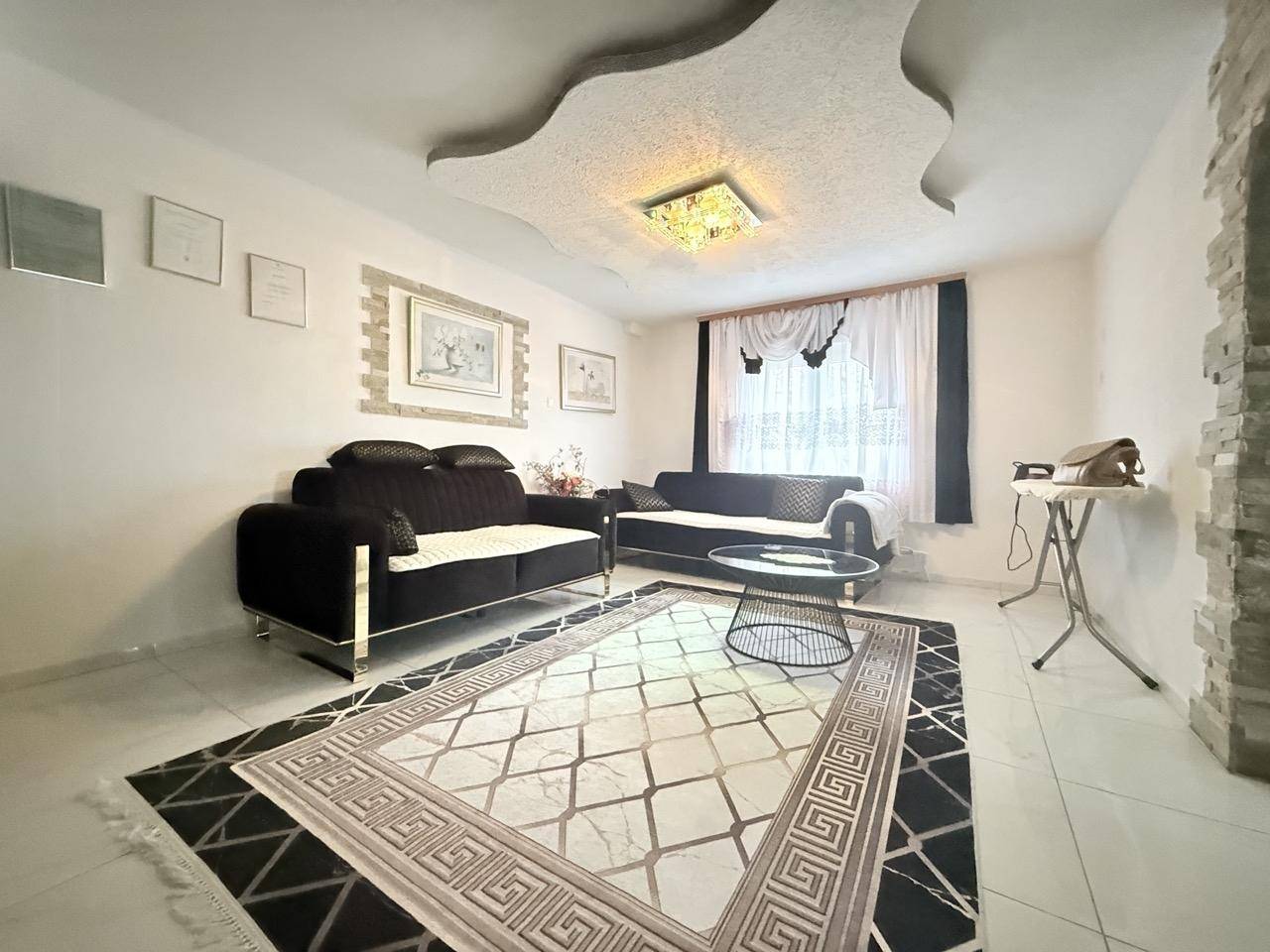 Gemütliches Wohnzimmer mit dunklen Sofas, Teppich und dekorativer Deckenbeleuchtung.