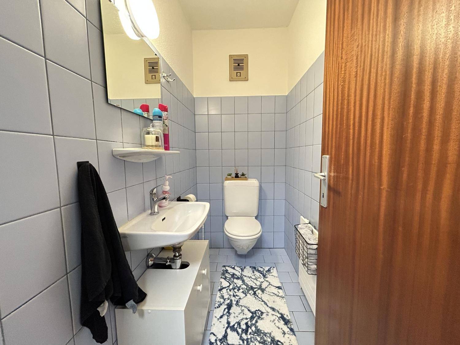 Helles Gäste-WC mit hellblauen Fliesen, Waschbecken und Toilette.
