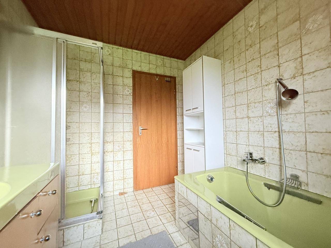 Badezimmer im Stil der 80er Jahre mit grüner Badewanne, Dusche und hell gefliesten Wänden.