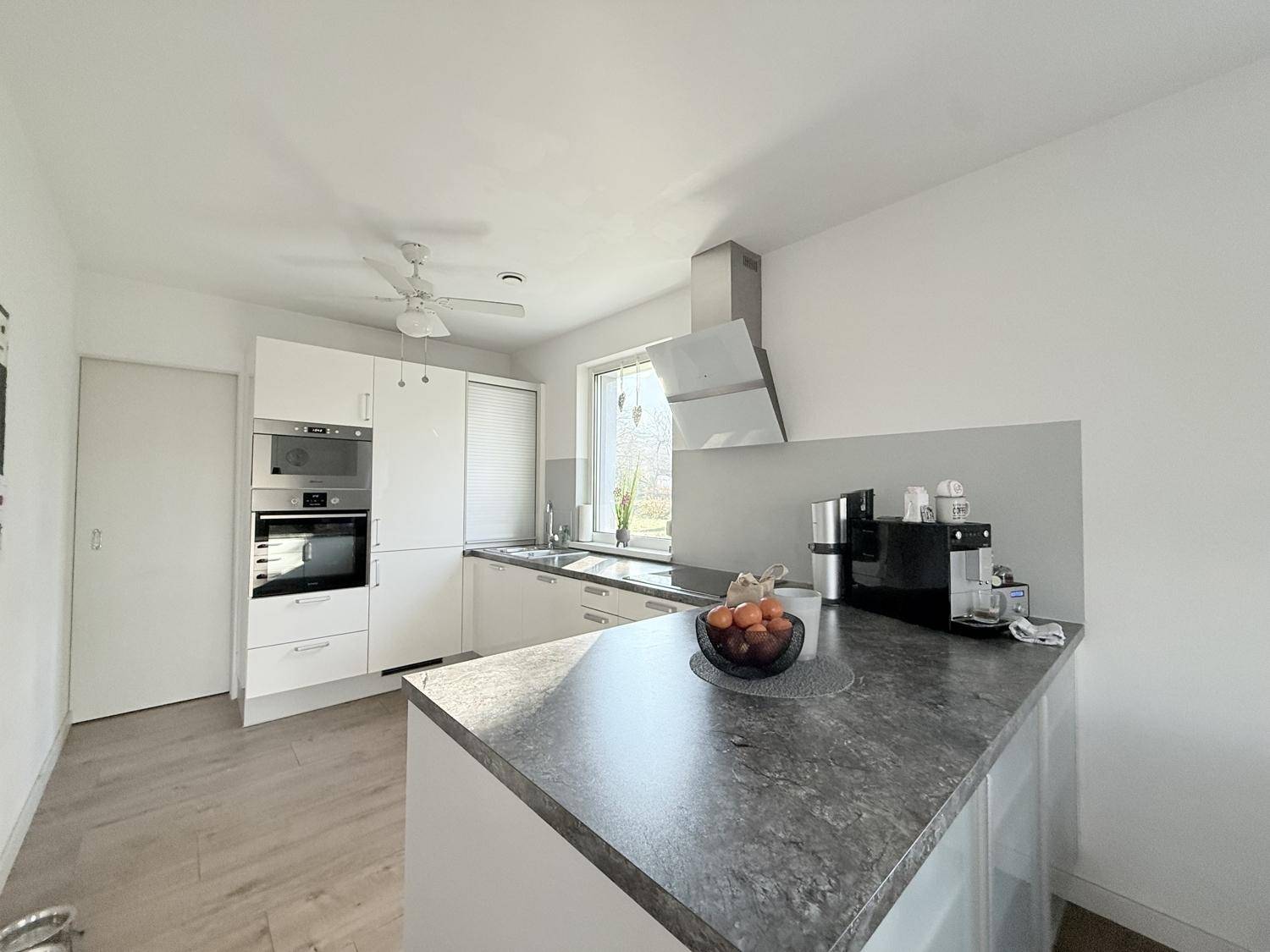 Moderne Einbauküche mit weißen Schränken, dunkler Arbeitsplatte und Fenster.