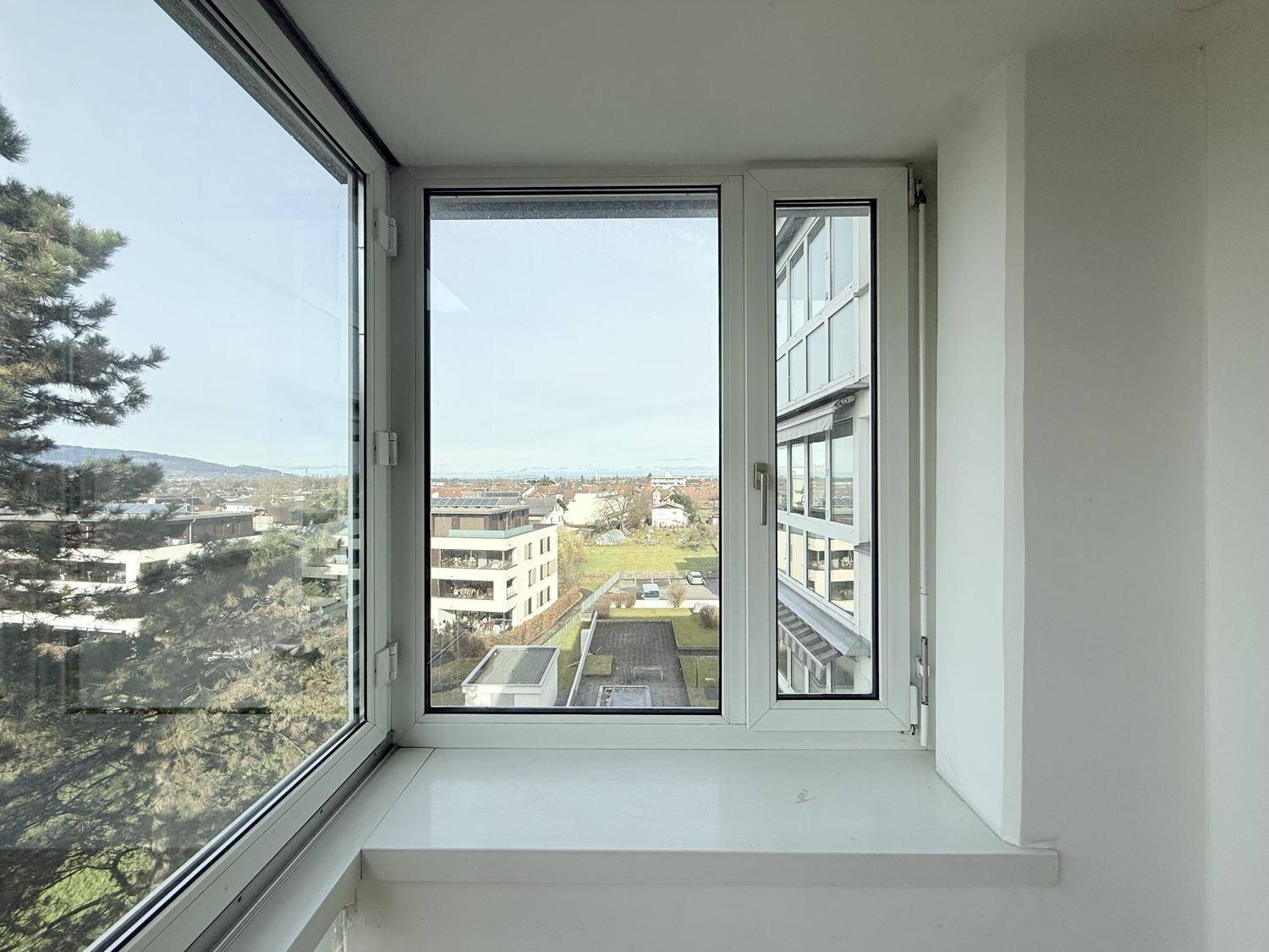 Fenster in der Loggia bietet einen klaren Blick auf moderne Gebäude und grüne Flächen in der Umgebung.